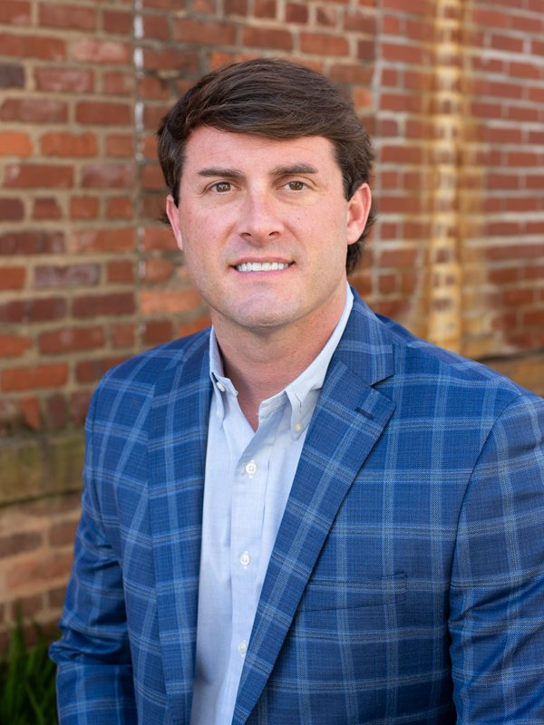 Smiling businessman in blue plaid suit jacket standing against brick wall background