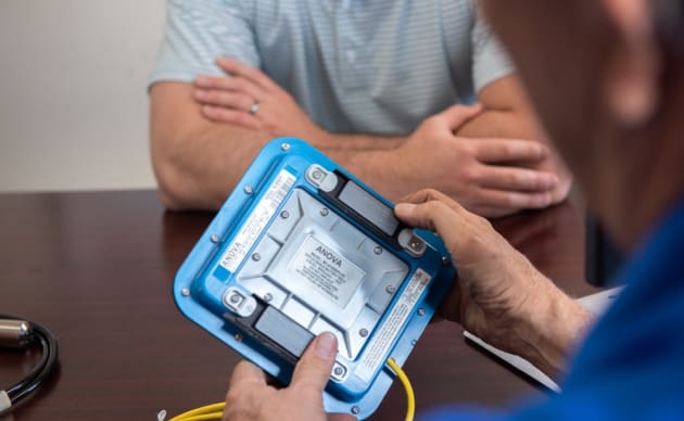 Doctor using handheld medical device to examine patient in clinic, close-up of hands