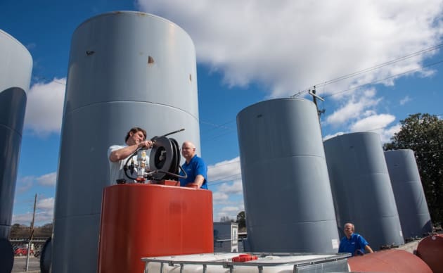 Technicians working on industrial tanks at manufacturing plant on partly cloudy day
