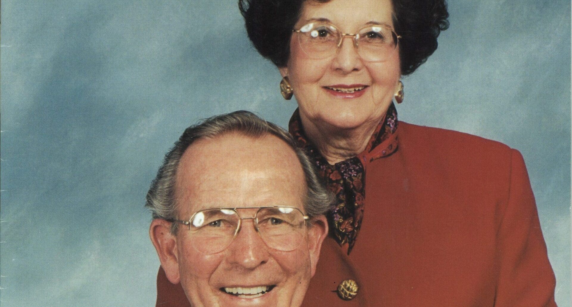 Smiling elderly couple in glasses and formal attire pose for portrait photograph